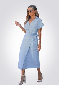 Vestido envolvente de rayas azul claro con mangas cortas, cintura ceñida y un diseño de longitud media. Lleva sandalias de tacón alto plateadas.