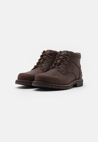 Bottines en cuir marron avec un bout rond, six œillets en métal, des coutures contrastées et une semelle en caoutchouc texturé.