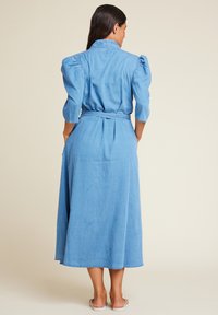 Denimkjole med belte i midjen, puffermer og midi-lengde. Har en lys blå farge og glatt tekstur.