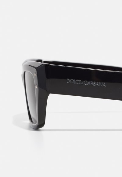Black sunglasses with a thick rectangular frame, glossy finish, and silver accents. "DOLCE & GABBANA" engraved on the arm.
