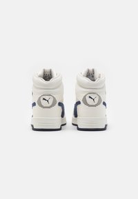 Wysokie sneakersy z białą skórzaną cholewką i granatowymi zamszowymi akcentami. Logo PUMA z tyłu, fakturowana cholewka i wyściełany kołnierz.