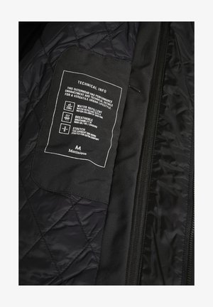 Intérieur d'une veste matelassée noire avec une étiquette comportant un texte blanc. Les détails incluent des propriétés déperlant, respirant et extensible.
