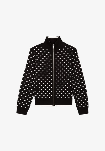 Cardigan noir à fermeture éclair avec un motif de petits cœurs blancs. Le tissu est texturé avec des poignets côtelés et un col montant.