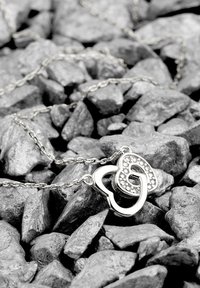 Sølv halskæde med to sammenflettede hjerteformer, hvoraf den ene har små klare ædelsten, som hviler på teksturerede sorte sten.