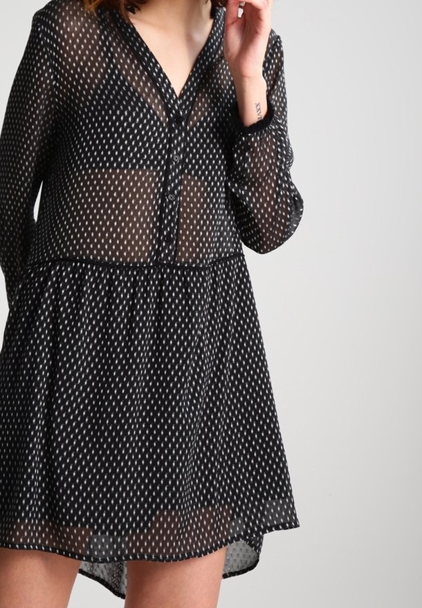 Robe noire transparente avec un devant à boutons, des manches longues et une taille froncée. Présente un motif de diamants blancs sur toute sa surface.