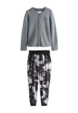 Grå cardigan med knapper og broderet logo, kombineret med sorte joggerbukser med hvide blomstermønstre og fugle.