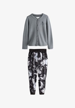 Grå cardigan med knapper og broderet logo, kombineret med sorte joggerbukser med hvide blomstermønstre og fugle.