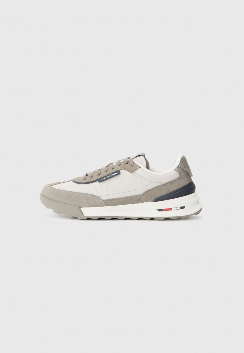 Grey and white sneakers featuring a mix of suede and textile. Contrasting navy and red accents, with a textured rubber sole and laces.