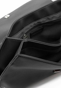 Interno di una borsa a mano in pelle nera che mostra una tasca con cerniera e due scomparti principali. Texture liscia con una grana sottile, dettagli in argento.