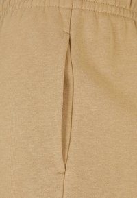 Joggers beige con cinturilla elástica y bolsillo lateral, confeccionados en suave tela de algodón, con una textura lisa y costuras elegantes.