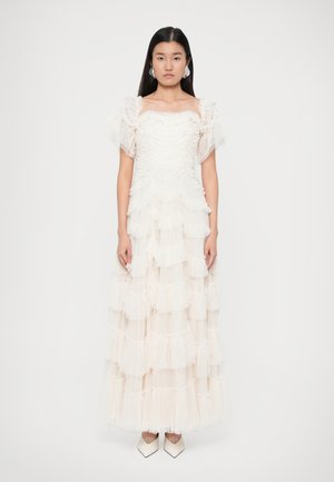 Robe blanche à volants en tulle avec des couches froncées et des manches courtes bouffantes. Le modèle porte des talons blancs à bout pointu.