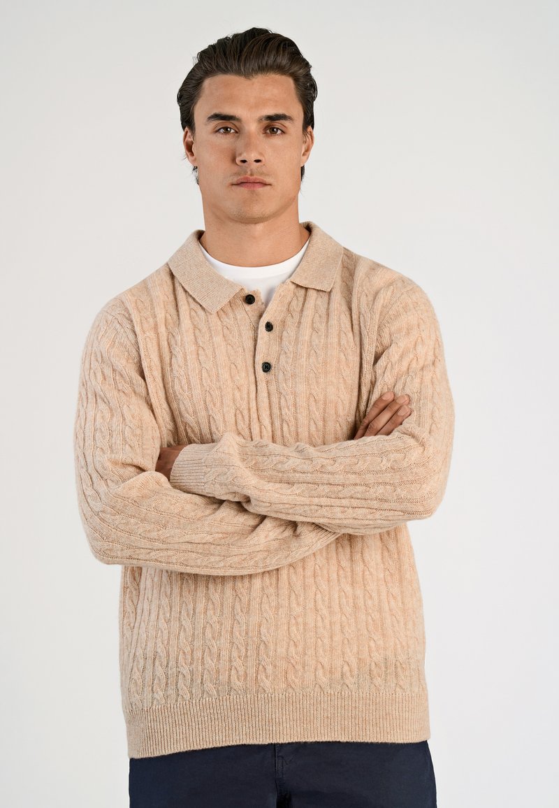 Beige kabelstickad tröja med krage, tre svarta knappar och ribbade ärmslut, med en avslappnad passform och strukturerad textil.