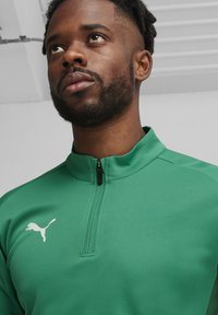 Groen sportjack met rits en opstaande kraag, gemaakt van soepel materiaal, met een klein wit Puma-logo op de borst.