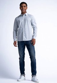 Lichtblauw overhemd met een geometrisch patroon, gecombineerd met donkere jeans en witte sneakers. De pasvorm is casual, met een moderne kraag.