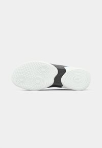 La semelle de la chaussure présente une base en caoutchouc blanc avec un grip texturé, un caoutchouc noir contrastant au centre, et comprend des éléments de traction circulaires.