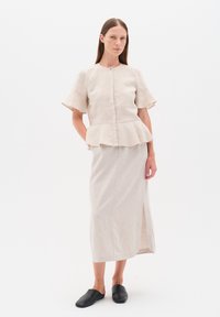 Vaalea beige pellavakankaasta tehty peplum-toppi, jossa on lyhyet hihat ja edessä nappikiinnitys, yhdistettynä yhteensopivaan midi-hameseen, jossa on sivureikä. Mustat puukengät.