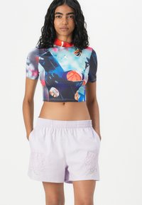 Lyhythihainen crop-top, jossa on värikäs printti koripalloista sinisellä taustalla. Laventelin väriset shortsit, joissa on brodeerattu kuvio ja joustava vyötärö.