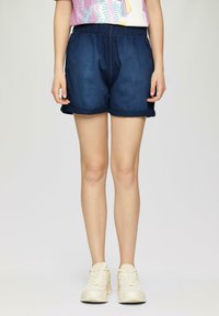 Shorts en denim bleu foncé avec une taille élastique, poches latérales et ourlets retroussés, associés à des chaussures de sport de couleur claire.