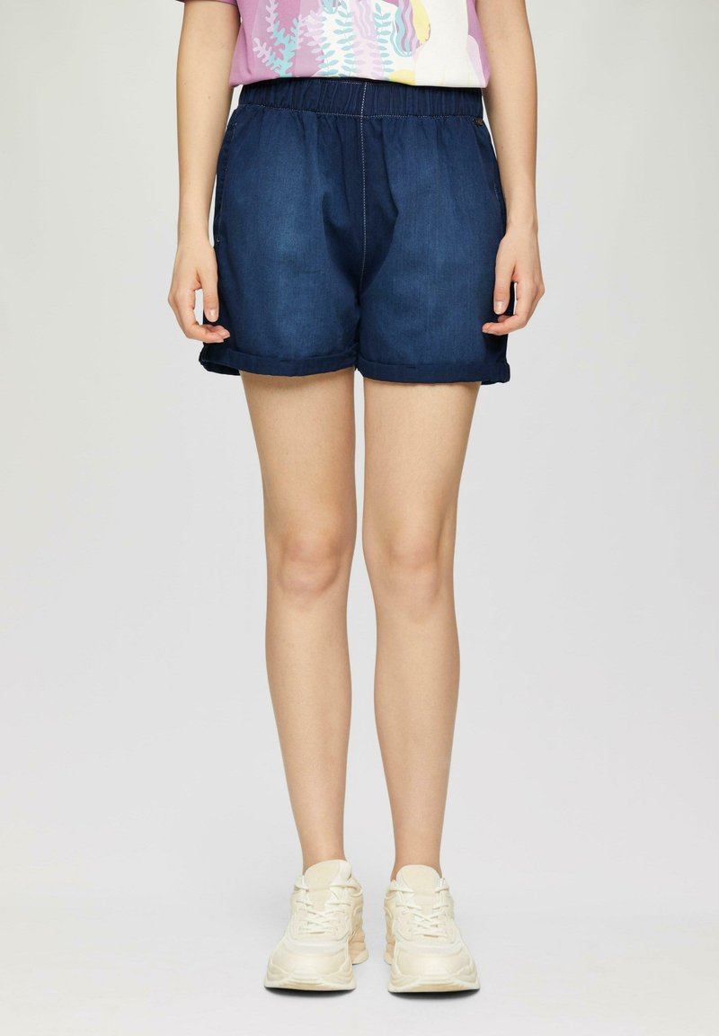 Shorts en denim bleu foncé avec une taille élastique, poches latérales et ourlets retroussés, associés à des chaussures de sport de couleur claire.