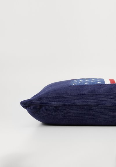 Mørkeblå dekorativ pude med et tekstureret strikket stof, som præsenterer et lille amerikansk flag-design i rød, hvid og blå på den ene side.