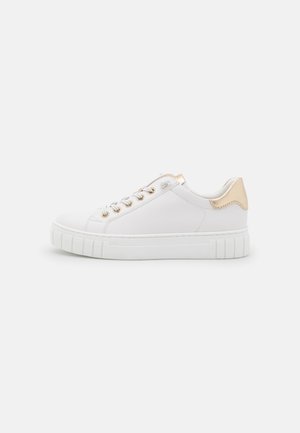 Hvid lavtop-sneaker med guldøjne og gulddetalje på hælen, flad tyk sål og hvide snørebånd på en ensfarvet baggrund.