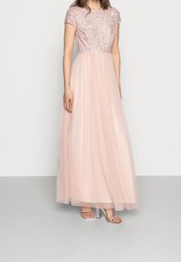 Vestido de noche rosa claro con un corsé de lentejuelas y falda de tul, con escote redondeado y mangas cortas. Sandalias de tacón alto transparentes.