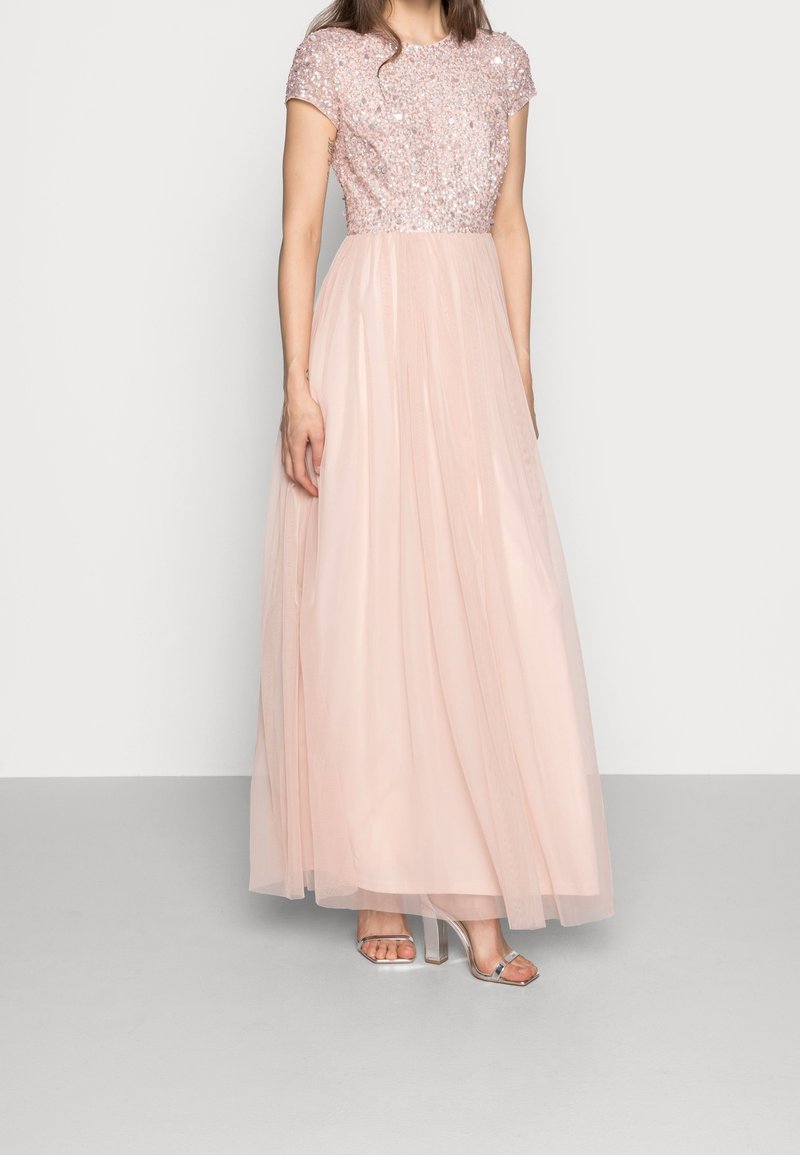 Vestido de noche rosa claro con un corsé de lentejuelas y falda de tul, con escote redondeado y mangas cortas. Sandalias de tacón alto transparentes.