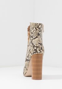 Stivaletto con tacco alto in un motivo pitonato beige e nero, dotato di una cerniera laterale e di un tacco marrone texturizzato.