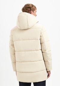 Beige gewatteerde jas met een capuchon, voorzien van gestikte panelen, een gladde textuur en een iets langere achterzoom.