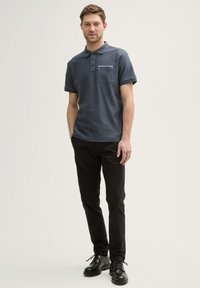 Granatowa koszulka polo z krótkim rękawem, trzema guzikami i kieszenią na piersi, w połączeniu z czarnymi spodniami slim-fit i czarnymi sznurowanymi butami.