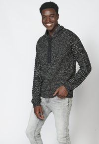Pullover a righe marled bianco e nero con colletto alto e dettagli con zip, abbinato a jeans grigi chiari con una vestibilità rilassata.