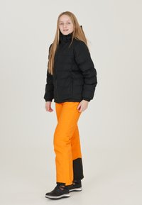 Svart puffjacka med hög krage, tillsammans med knallorange byxor med svarta accenter och hållbara kängor med vit sula.