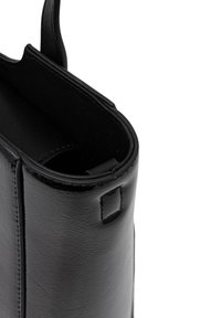 Gros plan sur le bord supérieur et la fixation de la poignée d'un sac à main en cuir noir avec des coutures visibles et une surface texturée.