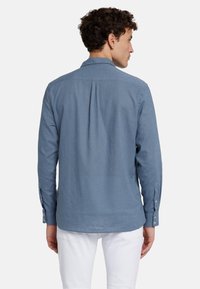 Camicia a maniche lunghe in cotone azzurro chiaro con plissettatura posteriore, polsini con bottone e colletto classico. Texture liscia e vestibilità su misura.
