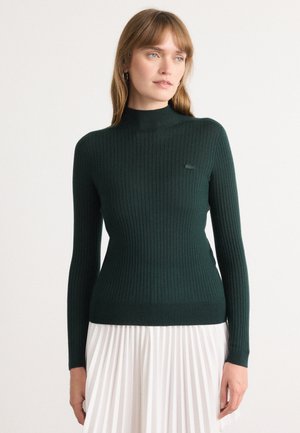 Mørkegrønn ribbestrikket turtleneck genser med lange ermer og slimfit-design. Har en liten logo på brystet. Teksturert strikkemateriale.