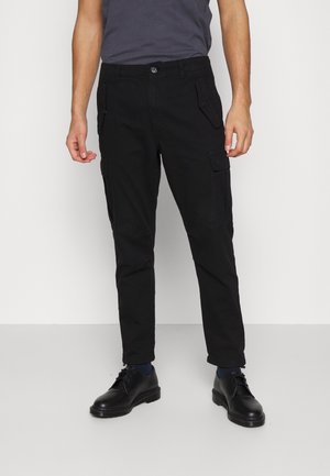 Pantalons cargo noirs en tissu résistant, dotés de poches latérales, d'une coupe droite et d'une fermeture à bouton. Portés avec des chaussures noires et un haut gris.