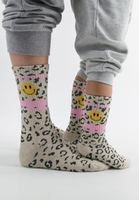 Leopardenmuster-Socken mit pinken Streifen, verziert mit gelben Smiley-Gesichtern. Hergestellt aus einem weichen, dehnbaren Stoff mit geripptem Textur.