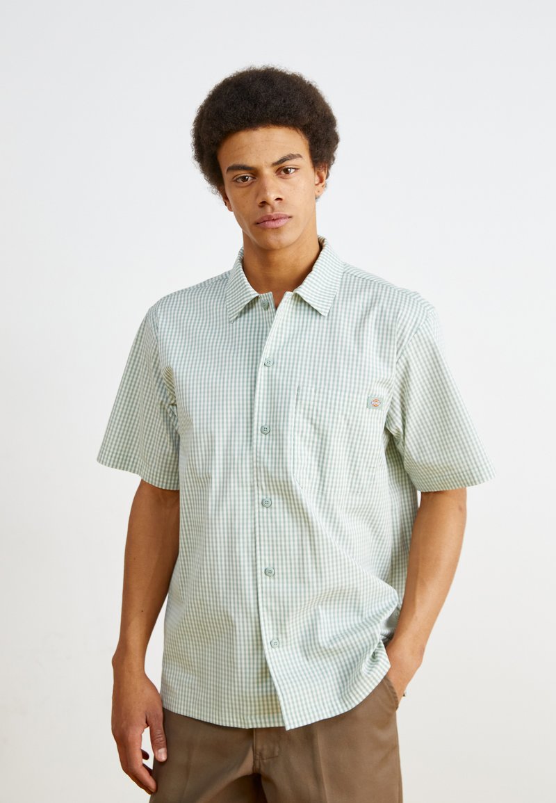 Kratký rukáv, kostkovaná košile v světle zelené a bílé barvě, s límcem na knoflíky, kapsou na hrudi a hladkým bavlněným povrchem.