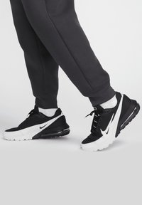 Svarta och vita träningsskor med nät- och syntetiskt ovandel, med en tjock sula, synlig luftdämpning och en framträdande Nike-logga.