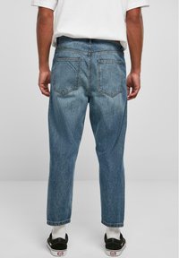 Jeans de mezclilla azul claro con un corte relajado, que cuentan con dos bolsillos traseros y un dobladillo con vuelta. Se llevan con zapatos negros y calcetines blancos.