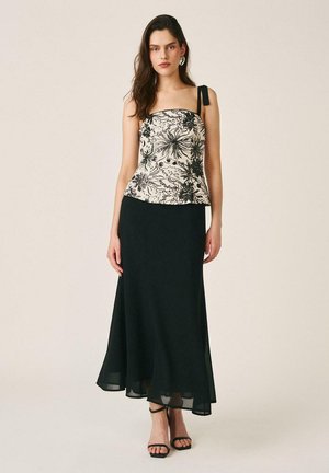 Mujer con un top strapless floral en blanco y negro con detalle de lazo y una falda negra fluida hasta los tobillos, junto con sandalias negras.