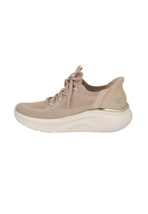 Zapatilla beige hecha de malla transpirable con diseño de cordones. Presenta una suela acolchada y un acento metálico en el talón para mayor soporte.