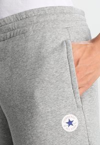 Pantalon de survêtement en coton gris avec une ceinture élastique, des poches latérales et un patch rond Converse All Star avec une étoile bleue.