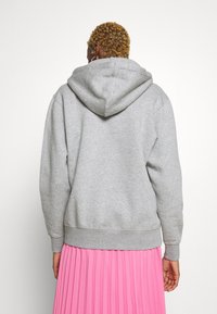 Felpa grigia con cappuccio e polsini a costine, realizzata in un tessuto morbido. Indossata con una gonna plissettata rosa, che mette in mostra un look a strati informale.