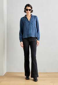 En dongeriskjorte i mørkeblått med spiss krage, frontplacket og puffede ermer. Sammen med svarte flagrende jeans og svarte ankelstøvler.