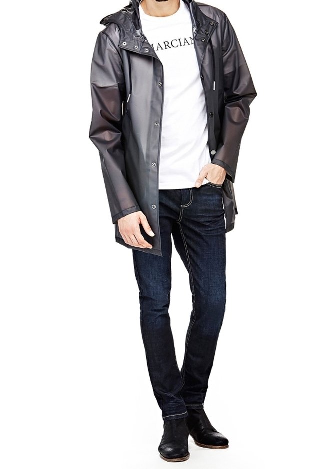 Impermeabile grigio con cappuccio, bottoni a pressione e tasche laterali, indossato sopra una maglietta bianca e jeans scuri. Stivali neri alla caviglia.