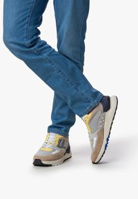 Sneaker in Grautönen, Gelb und Braun mit einem Mesh-Obermaterial, Wildlederakzenten und einer strukturierten Gummisohle, kombiniert mit blauen Denim-Jeans.
