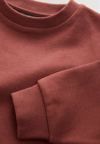 Bordeauxhuppari, jossa on ribbikuvioitu pyöreä kaula-aukko ja ribbikuvioidut hihansuut; sileä kankaankuva ja minimalistinen muotoilu, jossa on hienovaraisia värieroja.