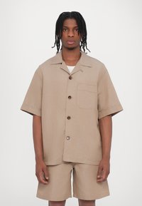Beige Kurzarmhemd mit Knopfleiste, einer Brusttasche und passenden Shorts, aus strukturiertem Stoff.