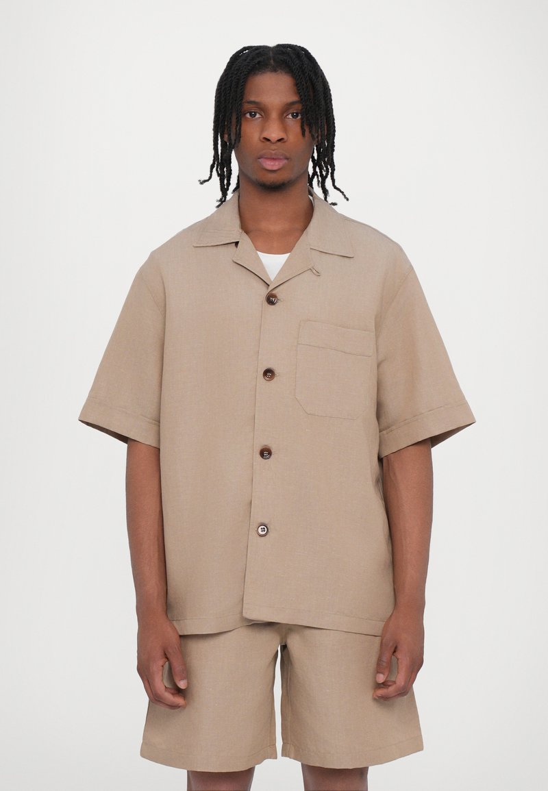 Beige Kurzarmhemd mit Knopfleiste, einer Brusttasche und passenden Shorts, aus strukturiertem Stoff.